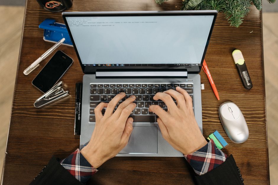 Overhead view of hands typing on laptop surrounded by office supplies on a wooden desk.