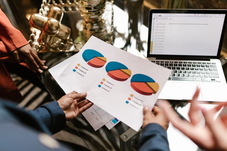 Professional hands holding pie chart data near laptop in modern office setting.
